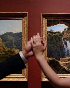 two people holding hands in front of paintings