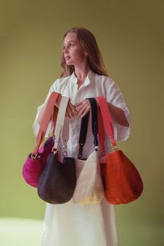 a woman is holding several purses in her hands and looking off to the side