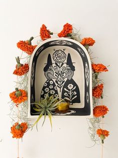 an art piece with orange flowers and plants on it, hanging from the side of a wall