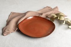 a brown plate sitting on top of a table next to a napkin and flower vase