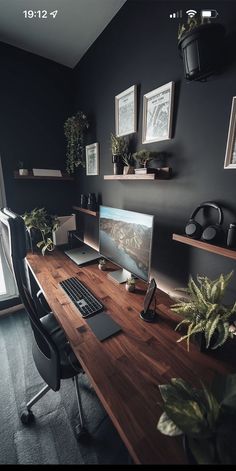 a desk with a computer on it in front of a window and some potted plants