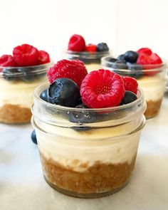 three desserts in small glass containers with berries and blueberries on top, sitting on a table