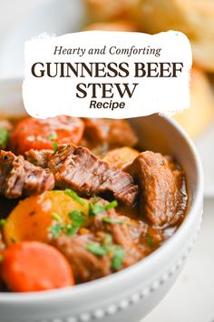 a white bowl filled with beef stew and carrots on top of a table next to bread