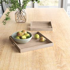 a bowl of fruit sitting on top of a wooden table next to two trays