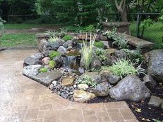 a garden with rocks, plants and water features in the center of the area that is bordered by a fence