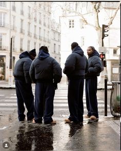 four men standing in the rain waiting to cross the street