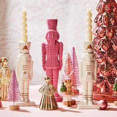 pink and gold christmas decorations are displayed on a table with white wall paper behind them