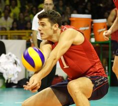 a young man holding a volleyball in his right hand and reaching for the ball with both hands