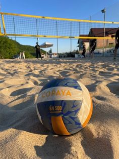 a beach volleyball ball sitting on top of the sand in front of a volley ball net