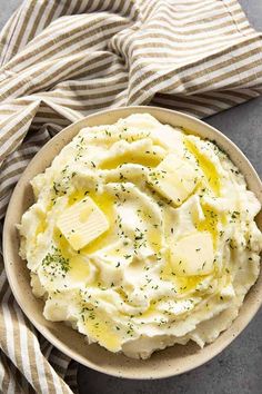 a bowl filled with mashed potatoes topped with butter and seasoning next to a striped napkin