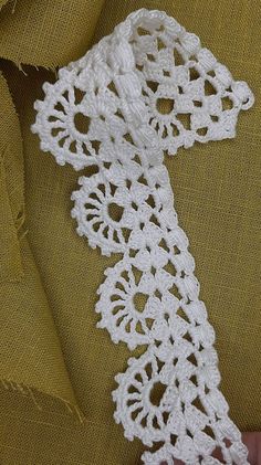 a white crocheted tie being held up by someone's hand on a yellow cloth