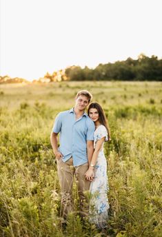 a man and woman standing in the middle of a field with tall grass at sunset