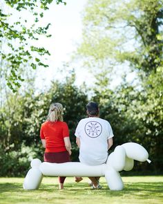 a man and woman sitting on a bench made out of balloons in the shape of a dog