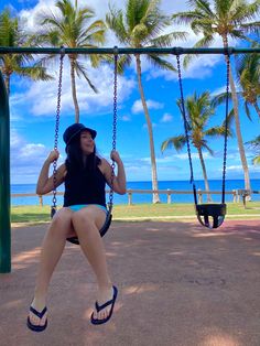 a woman sitting on a swing in front of palm trees with the ocean in the background