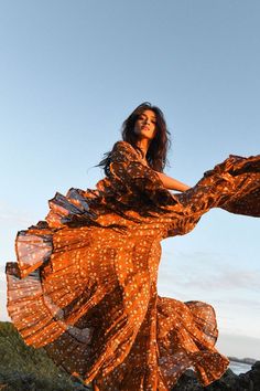 a woman in an orange dress standing on rocks with her arms spread out to the side