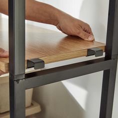 a hand is on the edge of a wooden table with metal bars and brackets attached to it