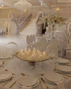 the table is set with many white plates and silverware, candles and flowers in vases