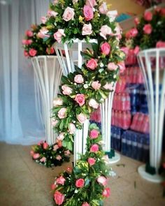 a cross with pink roses and greenery on the ground in front of other vases