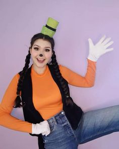 a woman in an orange shirt and black vest is posing with her hands on her hips