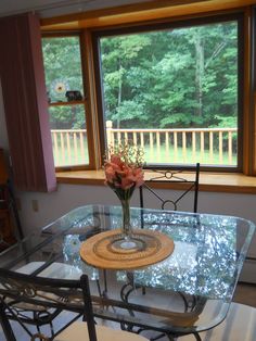 a glass table with flowers on it in front of a large window overlooking a wooded area