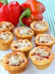 several mini pizzas on a white plate next to peppers