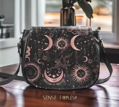 "Black Pink Boho Celestial Mystical Vegan leather Goth saddle bag, Sun Moon witchy crossbody handbag goth bag, hippies witch purse bag gift Small: 9.05\"(L) x 3.35\"(W) x 7.48\"(H) Large: 10.24(L) x 4.24\"(W) x8.66\" (H) .: 16.97 Oz. Made from high-grade Vegan leather with gold-tone hardware. .: Single zippered top inside closure, flap front closure with magnetic snap closure. .:Inner zipper pocket on back wall and a back zipper pocket. .:Cross body shoulder strap with adjustable length. .:Dimensions: 9.05\"(L) x 3.35\"(W) x 7.48\"(H). ❣️Actual colours may vary. This is due to computer monitors displaying colours differently and everyone can see these colours differently. We try extremely hard to ensure our end products are as close to the screen colour as possible, but please understand t Gothic Black Shoulder Bag For Festivals, Gift Black Saddle Bag With Adjustable Strap, Black Saddle Bag With Adjustable Strap As Gift, Black Saddle Bag With Adjustable Strap, Printify Ideas, Spiritual Accessories, Goth Bag, Leather Goth, Goth Purse