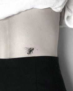 a small bee tattoo on the back of a woman's ribcage,