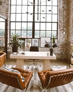 two leather chairs sitting in front of a white table next to a brick wall with large windows