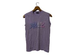 "1980's Vintage Florida Spring Break Beach SURF Vacation Sleeveless T-shirt Rad Beachwear Light Purple with Graphic Adult Medium Size: The tag says Adult Medium (vintage sizing runs small) Close to Small modern size Color: Light Purple Measurements: item lying flat,  17\" wide (armpit to armpit)  22\" length Brand: Sneakers Material: 500% cotton 50% Polyester made in USA Condition: This item is vintage and has been previously loved. There is a faintly bleahced spot at the bottom and a tiny hole Retro Crew Neck Tank Top For Summer, Vintage Sleeveless Tops For Summer, Vintage Tank Top For Spring Streetwear, Vintage Crew Neck Muscle Tee For Summer, Vintage Sleeveless Top For Beach, Vintage Crew Neck Tank Top For Summer, Vintage Cotton Muscle Tee For Summer, Vintage Sleeveless Top For The Beach, Vintage Tank T-shirt For Summer