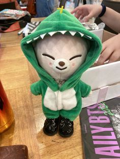 a stuffed animal with a green hoodie and black shoes on top of a wooden table