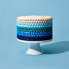 a multi - colored cake sitting on top of a white pedestal against a blue background