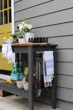 an outdoor table with towels, utensils and other items on it next to a yellow door