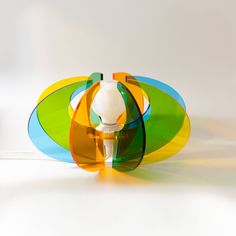 an object made out of colored plastic on a white surface with light coming from behind it