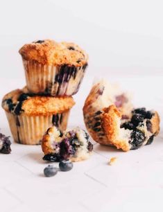 three blueberry muffins with one broken in half on a white countertop