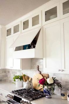 a kitchen with white cabinets and marble counter tops is pictured in this image, there are vases on the stove