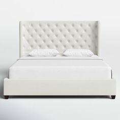 a white bed with an upholstered headboard and two pillows on the top