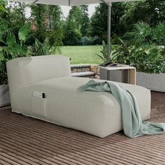 an outdoor lounge chair under an umbrella on the deck with potted plants in the background