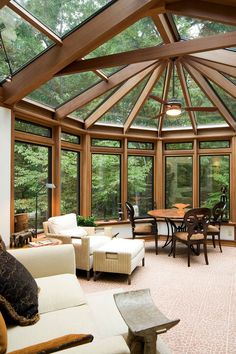 a living room filled with lots of furniture under a wooden roof covered in glass walls