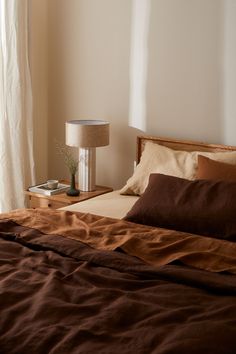 a bed with brown sheets and pillows in a bedroom next to a lamp on a nightstand