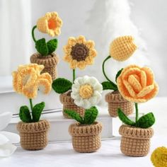 crocheted flowers are in small pots on a table with white and yellow decorations