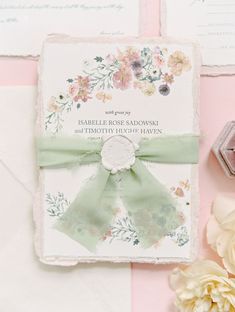 wedding stationery with green ribbon and flowers on pink table cloth, next to wax stamp