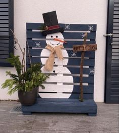 a snowman sitting on top of a wooden bench next to a potted plant