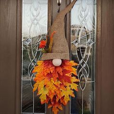 a scarecrow door hanger decorated with fall leaves and an orange hat on the front door