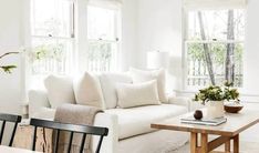 a living room filled with white furniture and lots of window sill space next to a wooden table