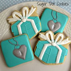 three decorated cookies sitting on top of a white plate with blue and silver gift boxes