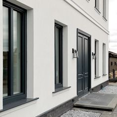 a white building with black windows and graveled walkway leading to the front door area