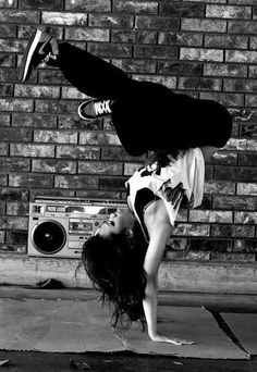 a woman is doing a handstand in front of a brick wall with her feet on the ground