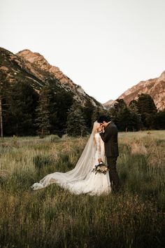 a bride and groom kissing in a field with mountains in the background at their wedding