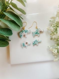 three pairs of earrings sitting on top of a white surface next to flowers and greenery