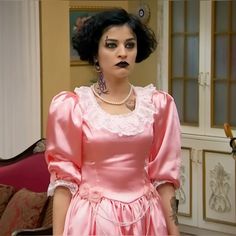 a woman in a pink dress with black lipstick on her lips is standing next to a couch